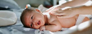 baby laying on bed while woman massaging his back